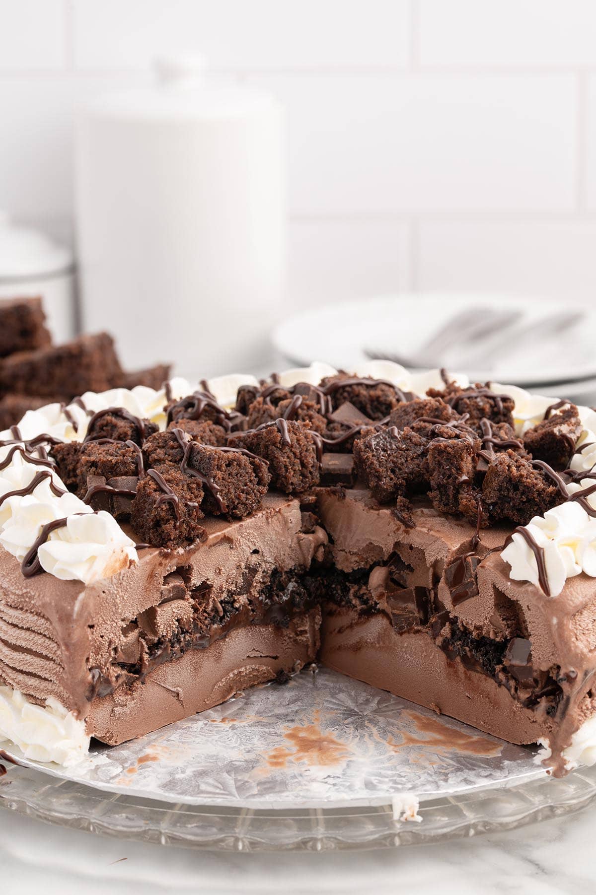 a sliced Dairy Queen Copycat Chocolate Ice Cream Cake with whipped cream and chocolate drizzle, topped with chopped brownies.