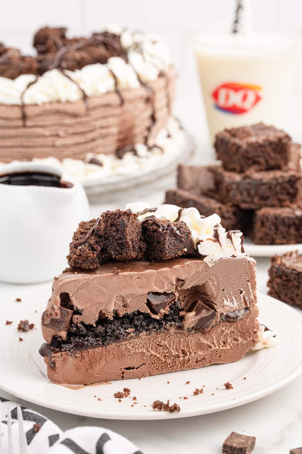 a slice of Dairy Queen Copycat Chocolate Ice Cream Cake on a plate with whipped cream and chopped brownies on top.