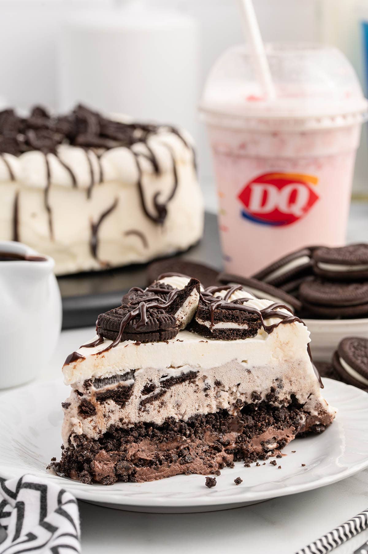 a slice of Dairy Queen Copycat Oreo Cookie Ice Cream Cake on a white plate with Dairy Queen takeout cup in the background. 