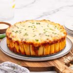 a Honeycomb Pasta Cake on a wooden board garnished with chopped basil.