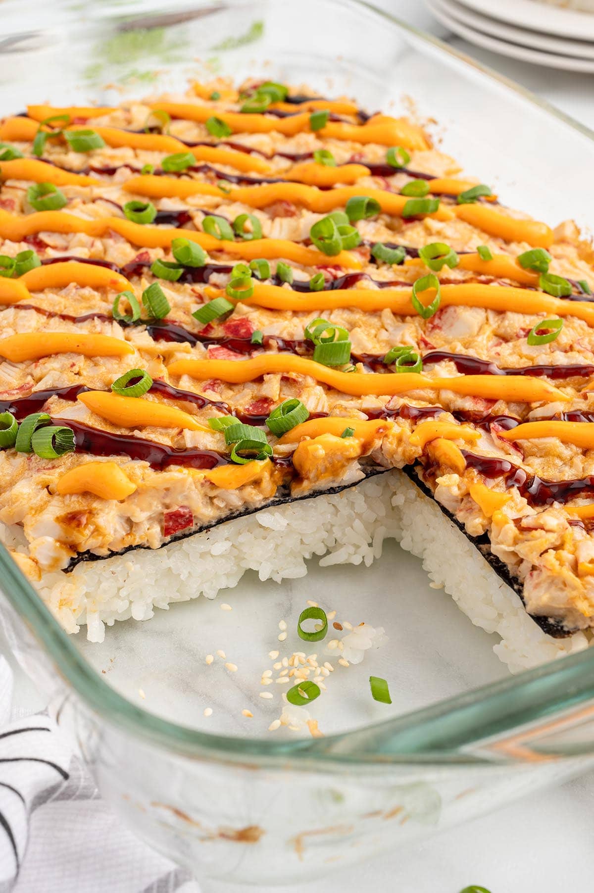 Sushi Bake in a baking dish garnished with sauces and sliced green onions.