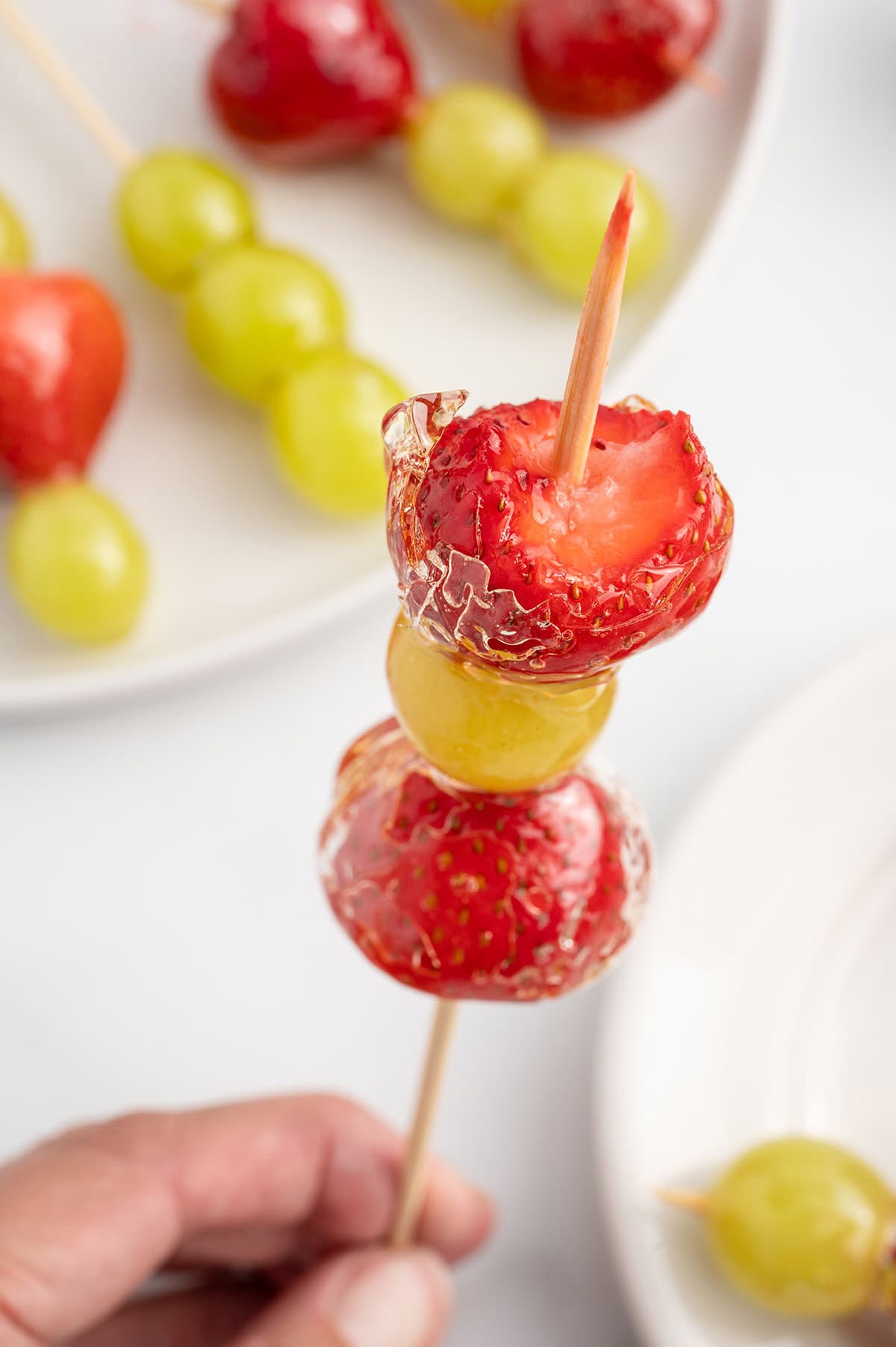 a skewer of Tanghulu with strawberries and grape coated in a shiny glaze.