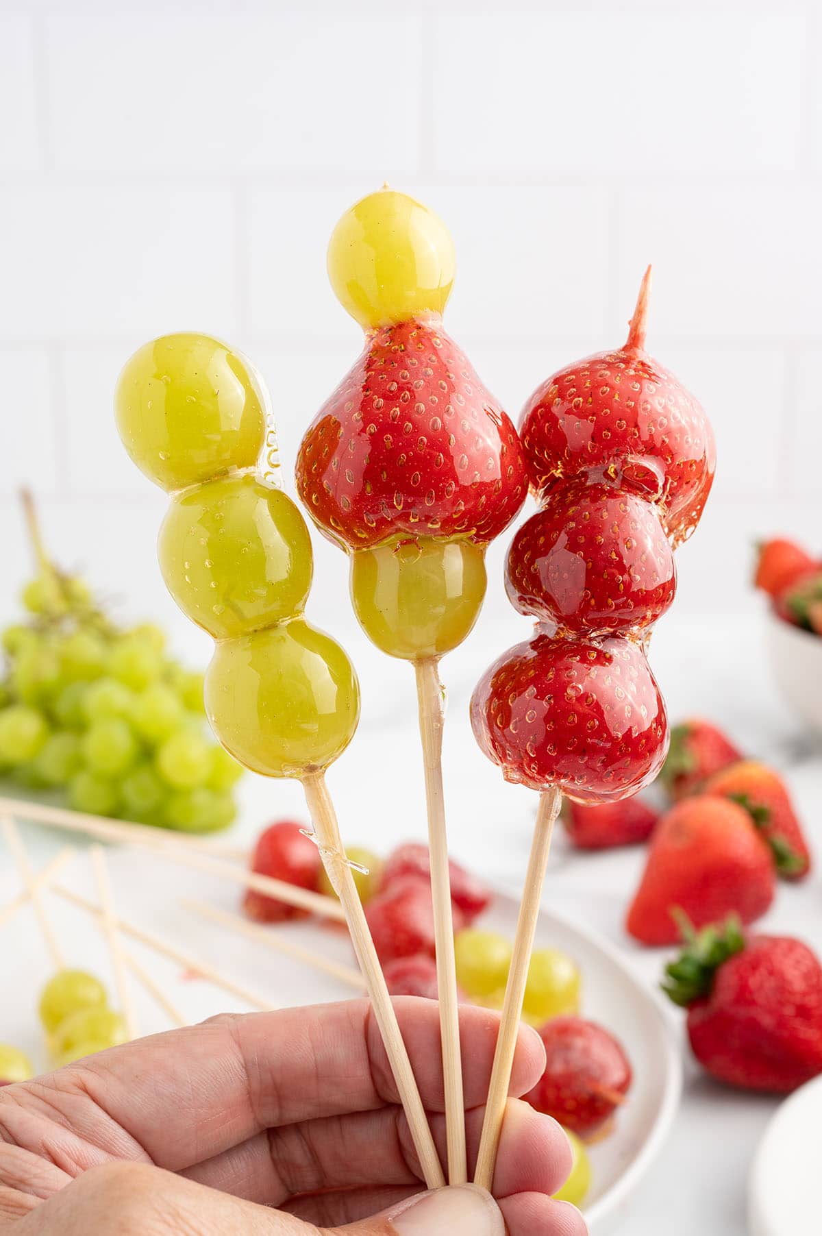 a hold hands three skewers Tanghulu coated in a glossy and hard candy shell.