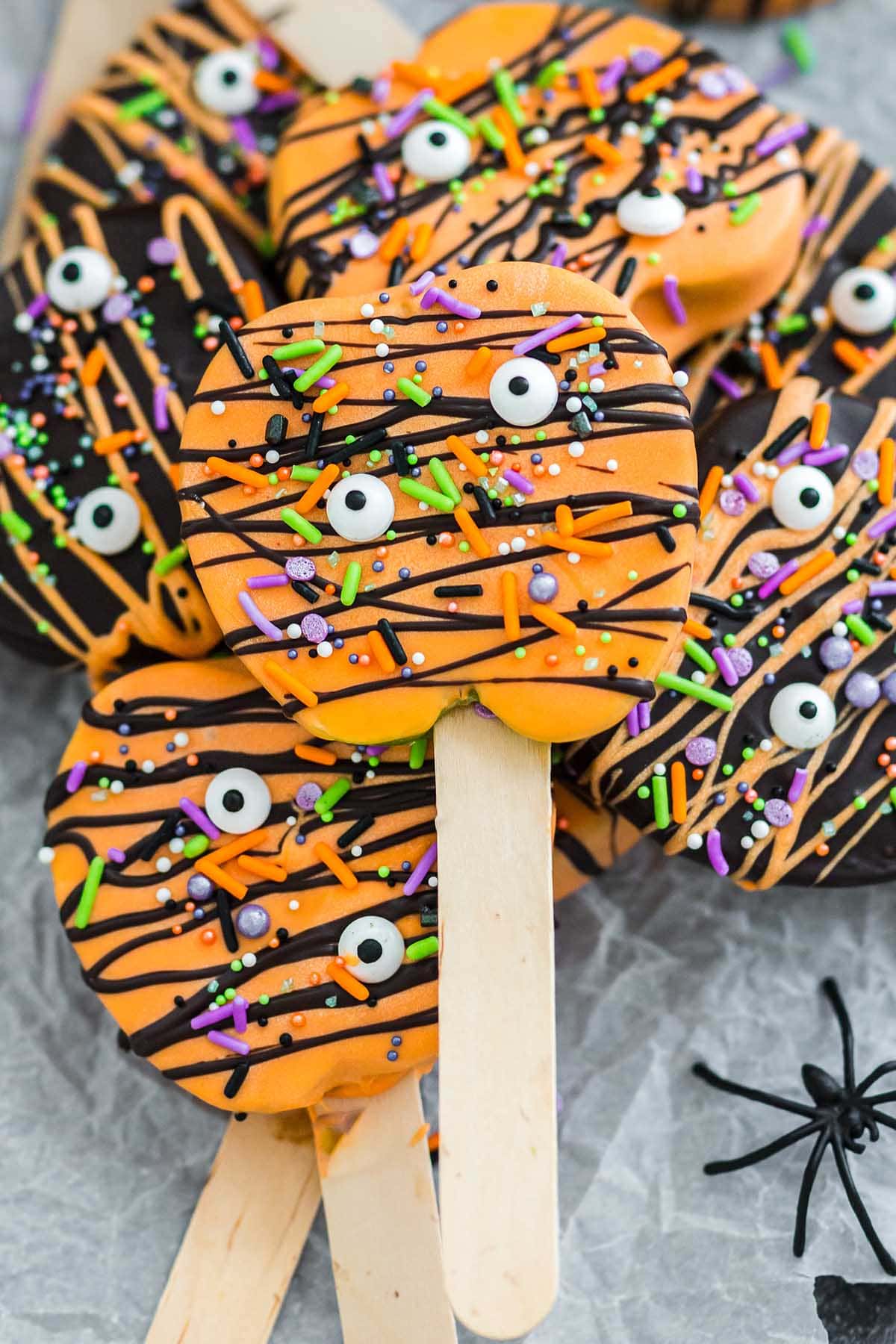 a couple of Halloween Chocolate Covered Apple Pops with colorful sprinkles, candy eyes and drizzle of black icing.