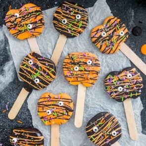 a couple of Halloween Chocolate Covered Apple Pops scattered over parchment paper.