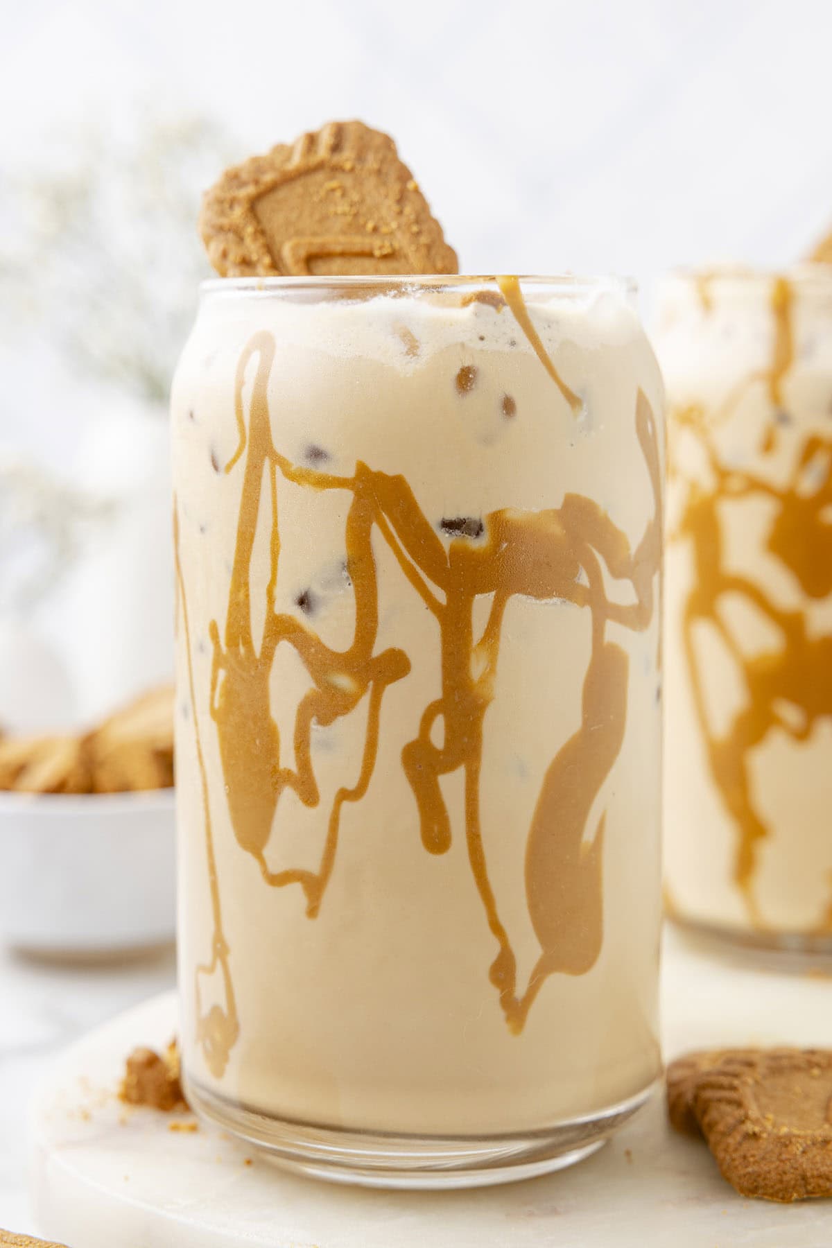 Iced Cookie Butter Latte in a clear glass with drizzle and cookie on top.