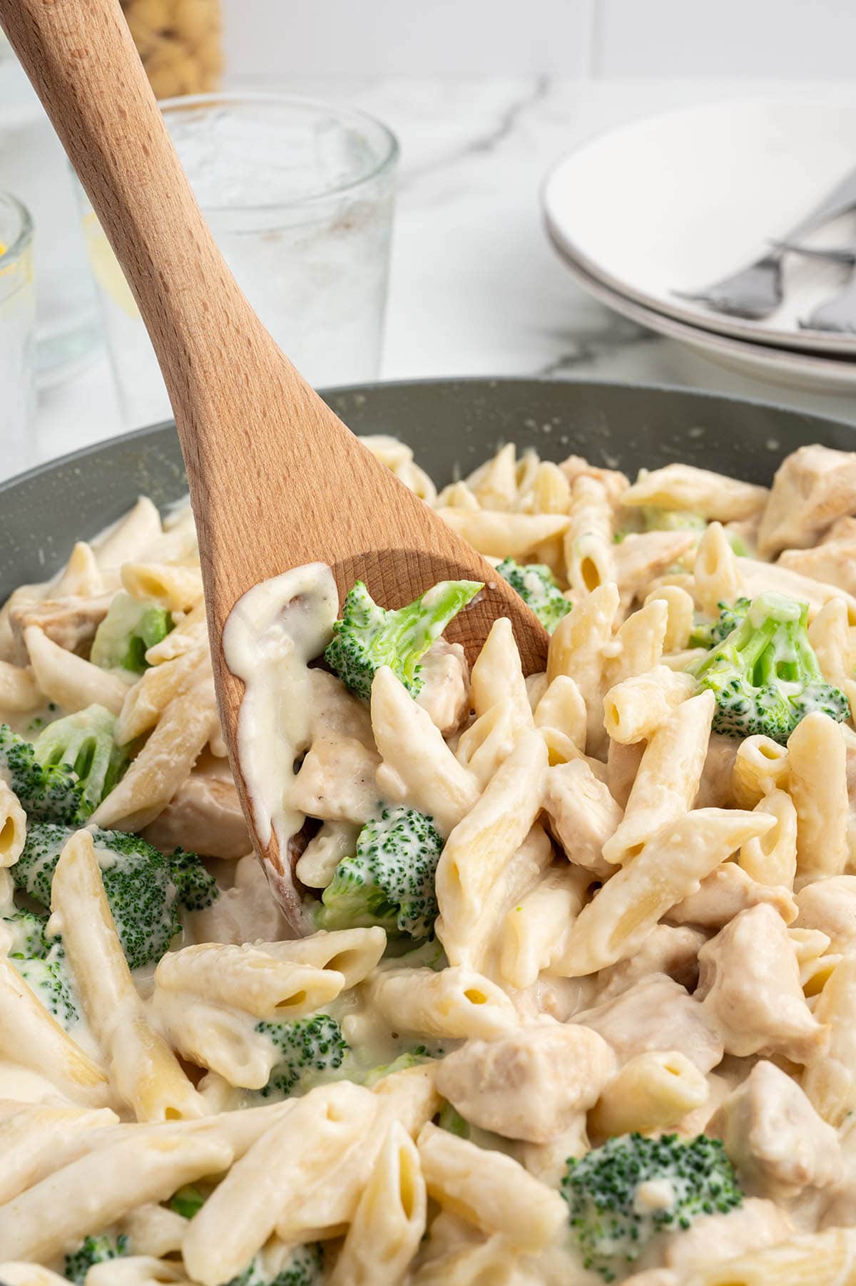 chicken and broccoli penne alfredo in a skillet with wooden spoon. 