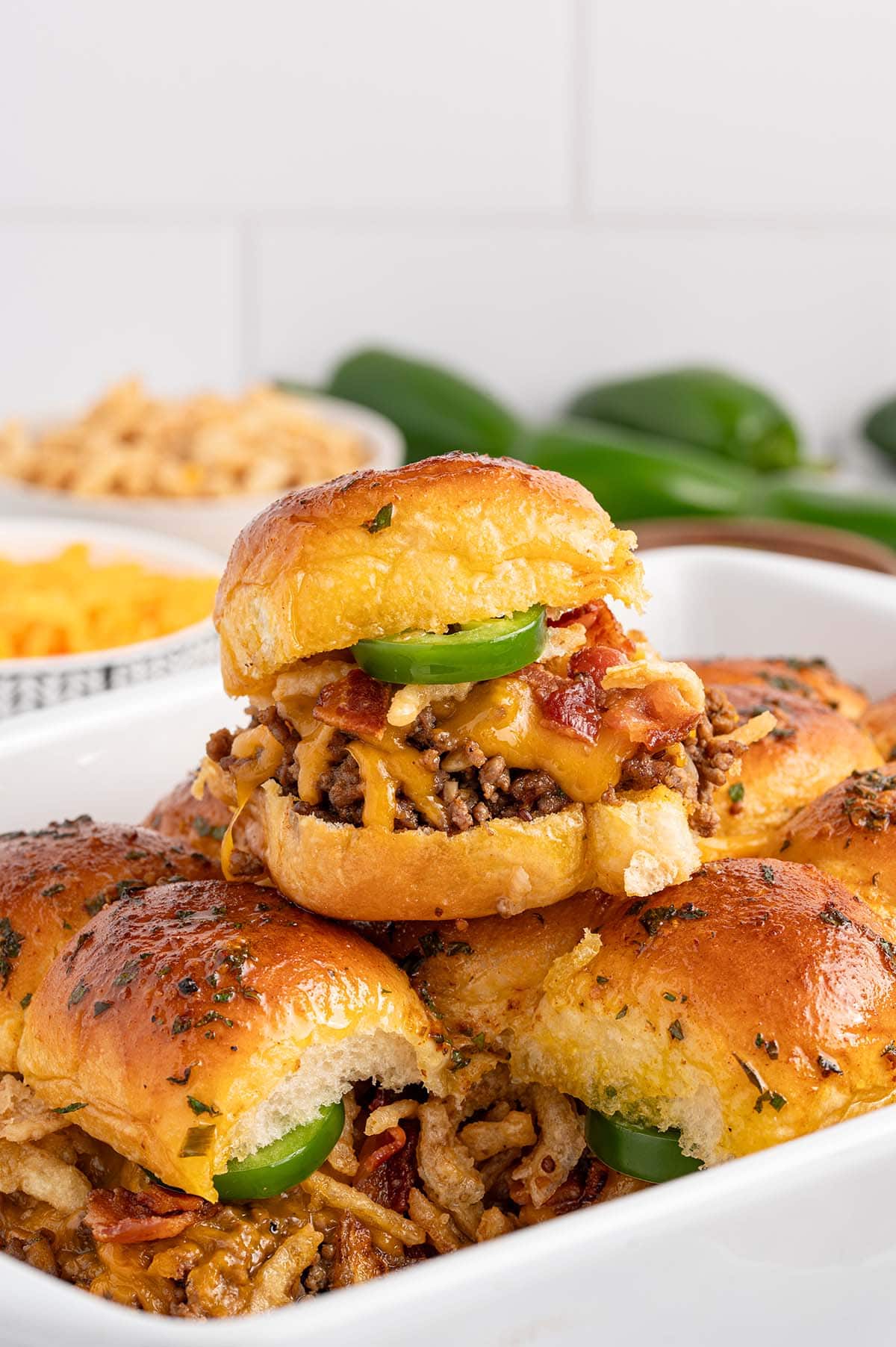 a stack of Cowboy Sliders with ground beef , melted cheese, bacon and jalapeno slices served on toasted buns.