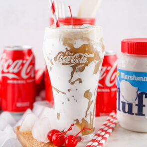 a glass of Fluffy Coke with coke cans and marshmallow fluff in the background.