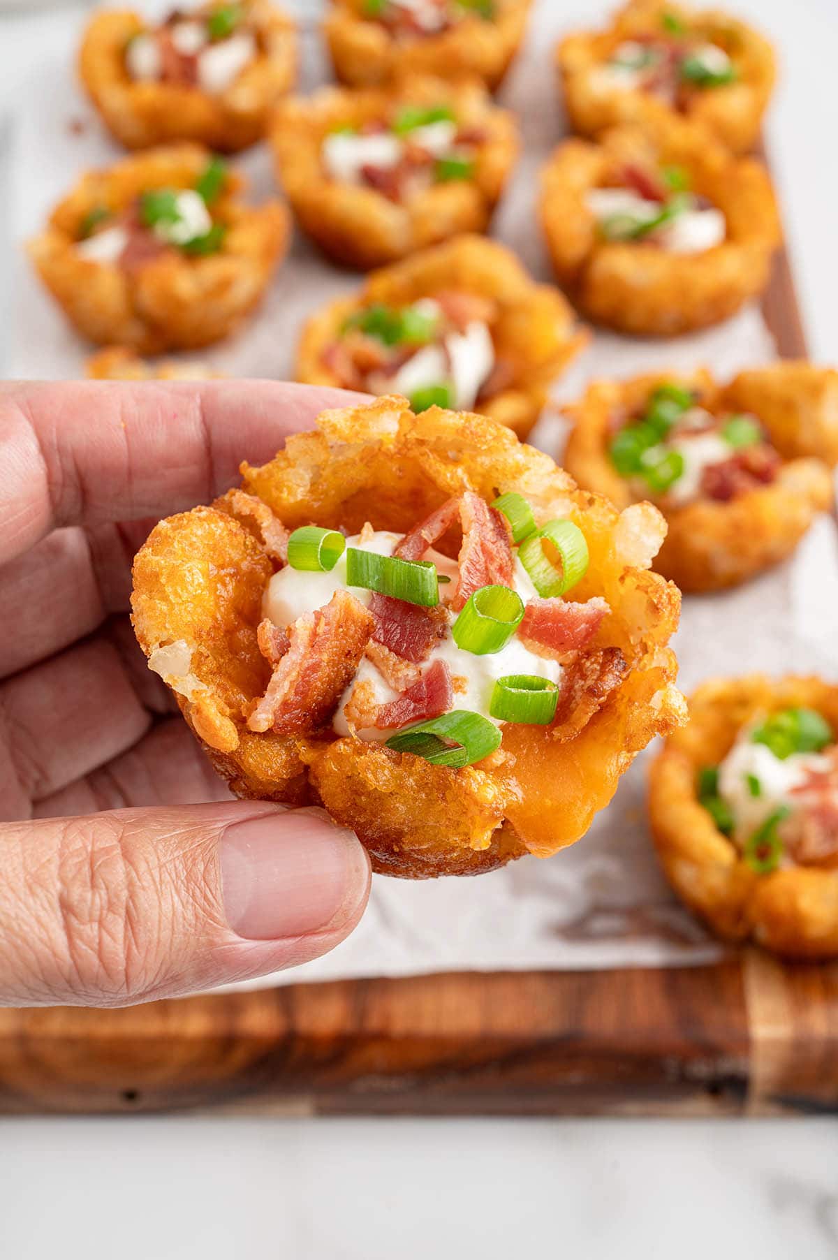 a hand holding a piece of Loaded Tater Tot Cups.