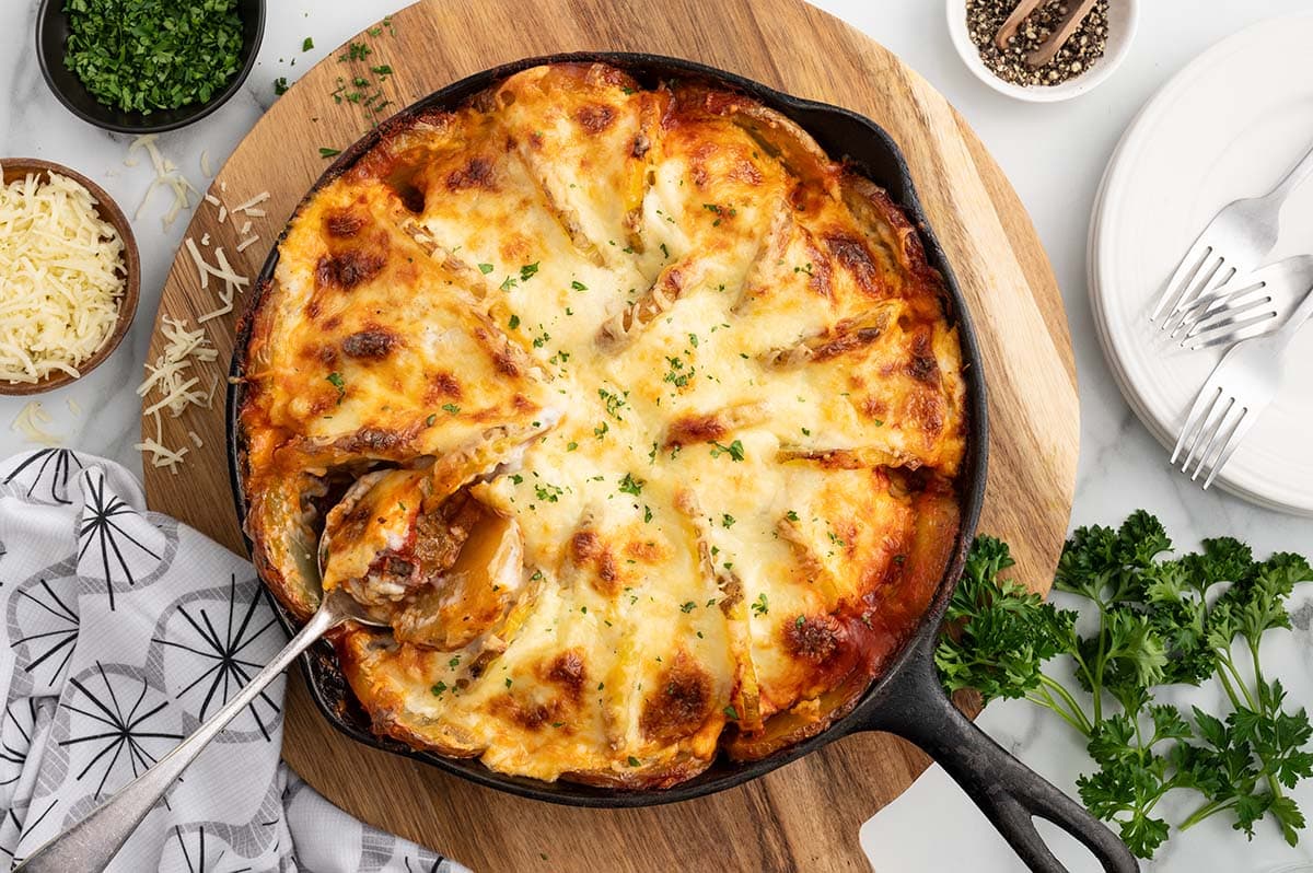 a cast iron skillet filled with Meatballs and Potatoes placed on a wooden board garnished with fresh parsley.