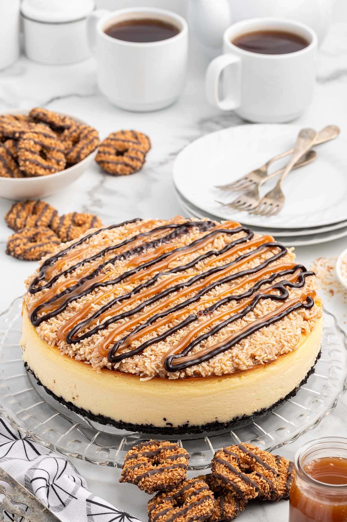 Samoa Cheesecake served on a glass plate topped with caramel and chocolate sauce. 