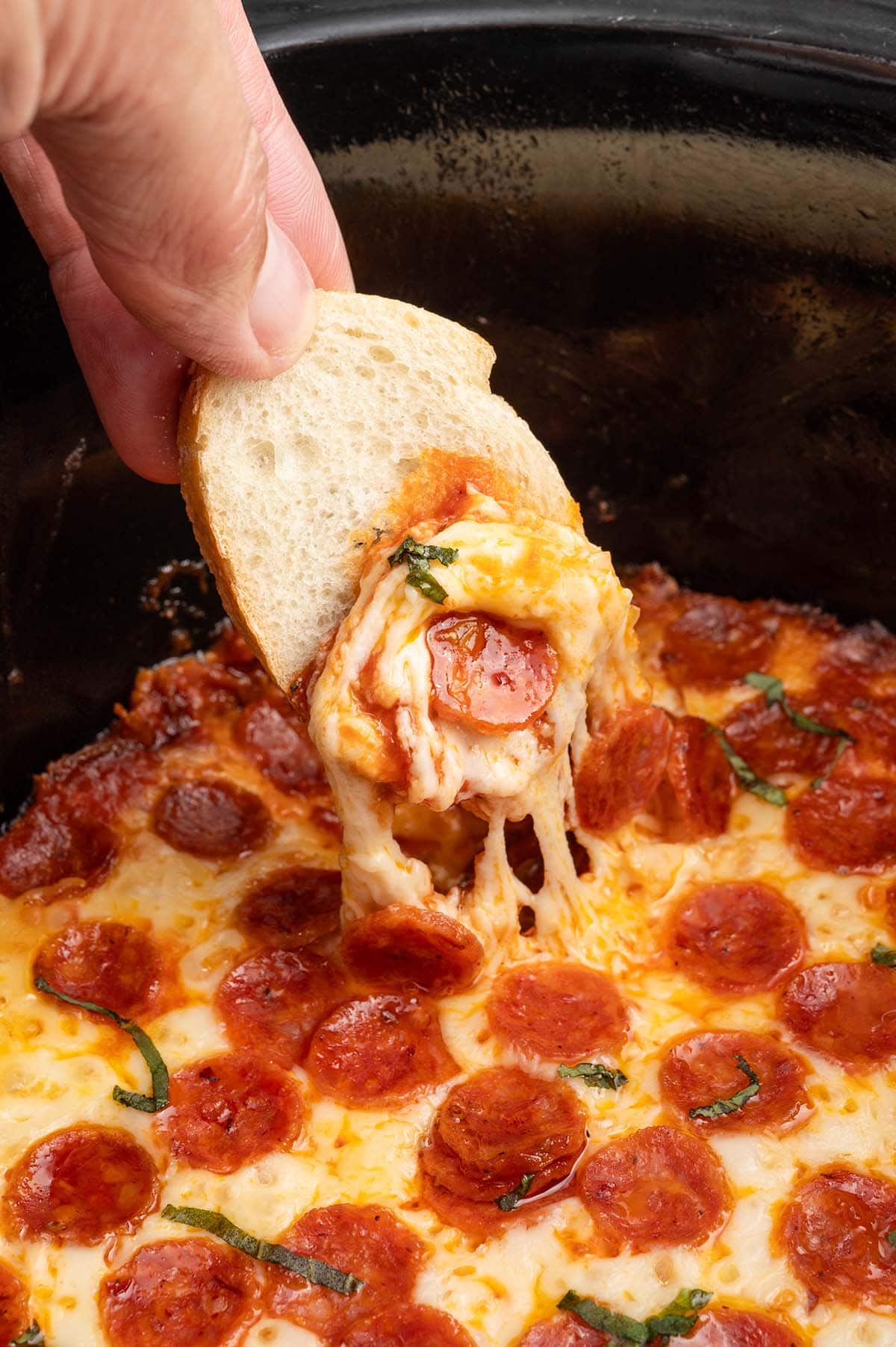 a sliced of bread being dipped into Crock Pot Pizza Dip.