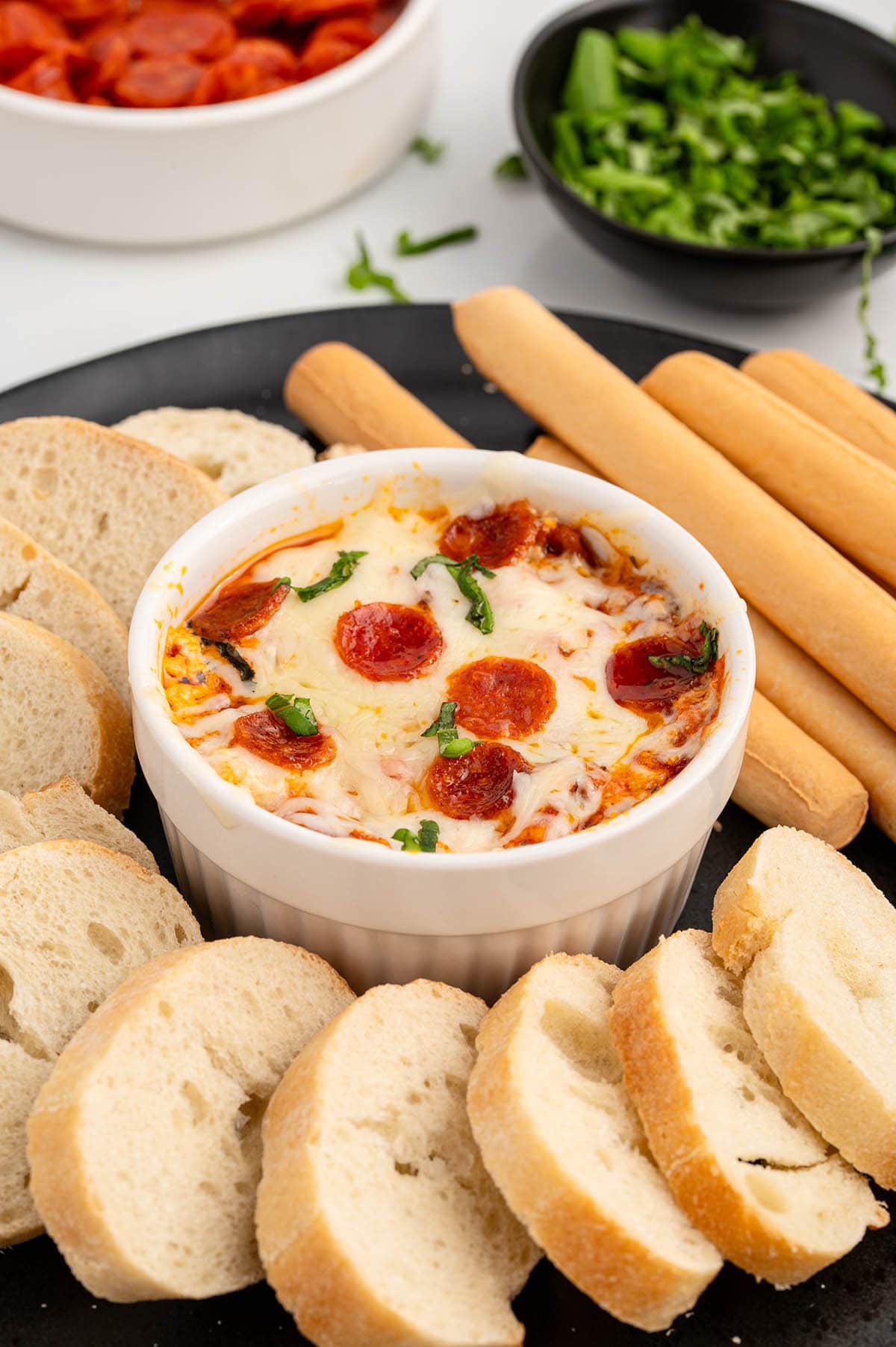 a bowl of Crock Pot Pizza Dip surrounded by bread and breadsticks on a plate.