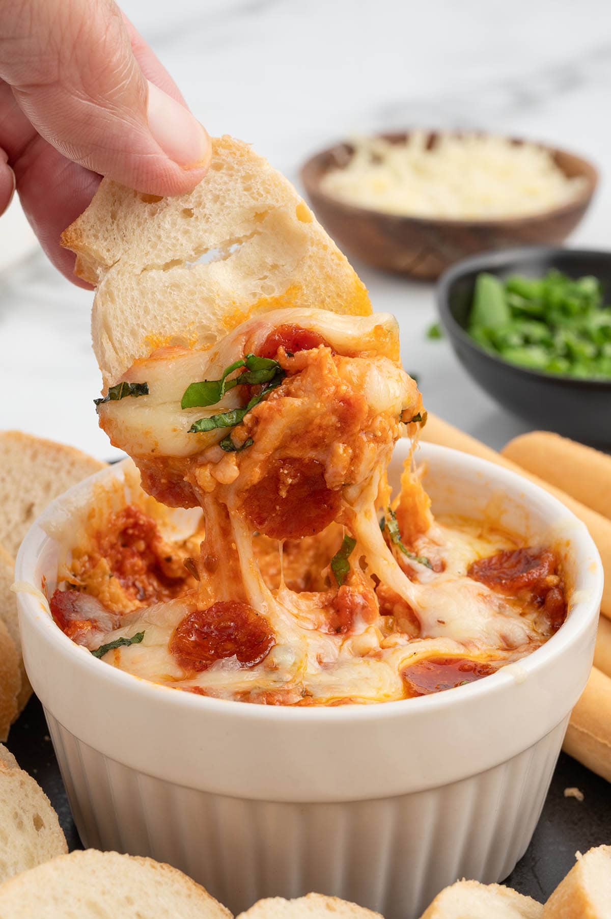 dipping a piece of bread into a white ramekin filled with Crock Pot Pizza Dip.