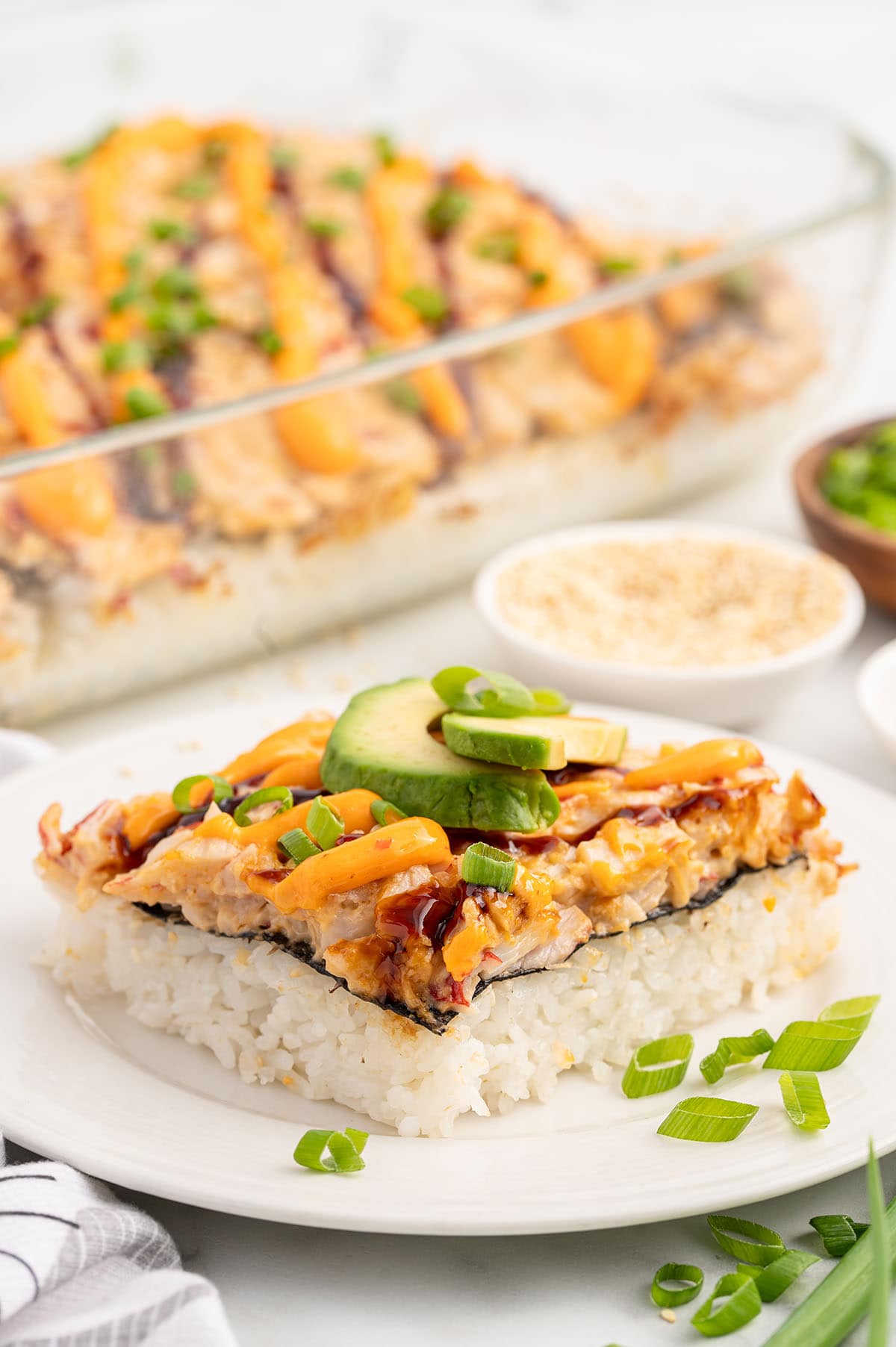 a slice of Sushi Bake on a white plate topped with chopped green onions.