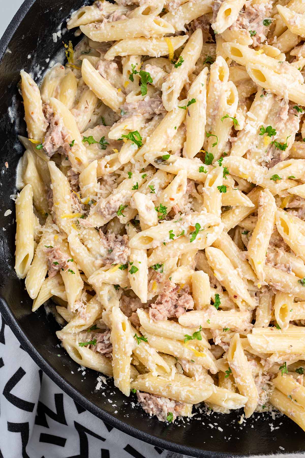 Tuna Pasta in a skillet garnished with chopped parsley and grated parmesan cheese.