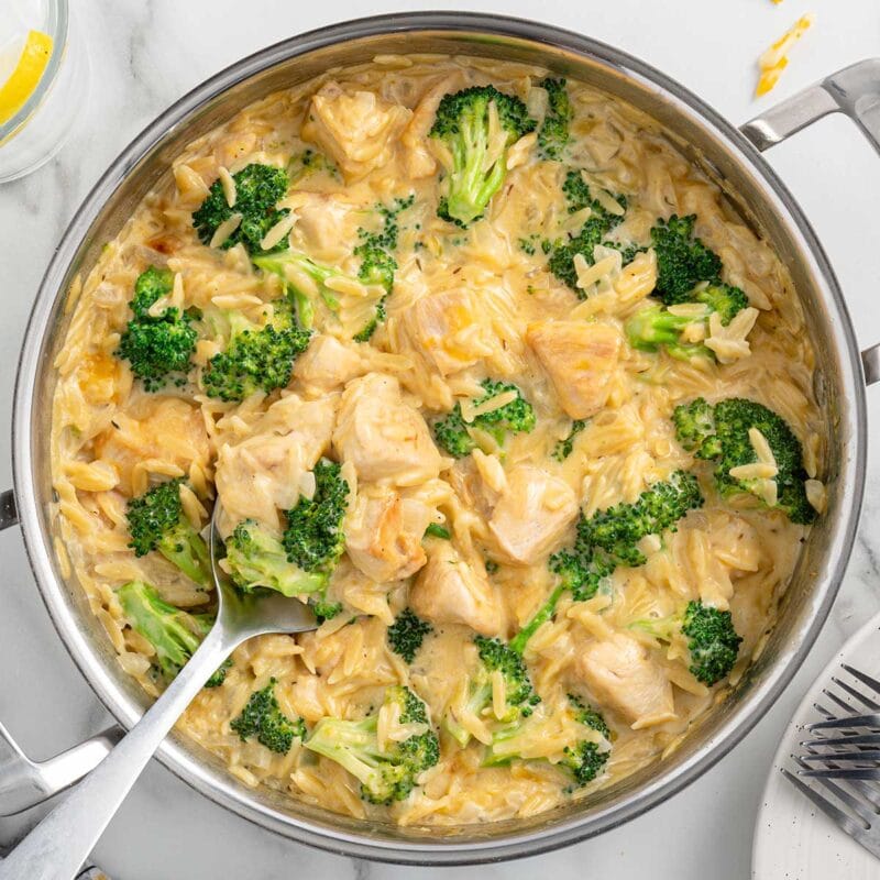 a large skillet filled with cheesy chicken orzo and broccoli florets.