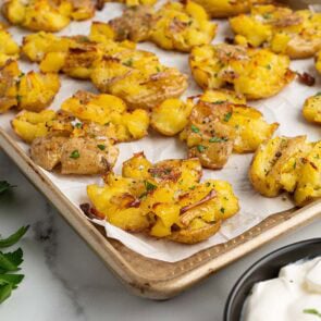 Crispy smashed potatoes on a baking sheet with parsley and sour cream.