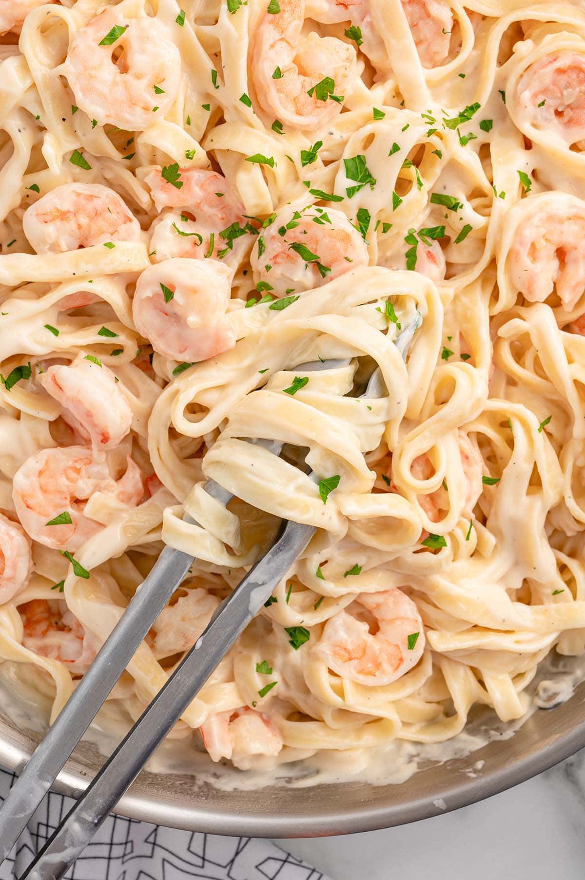 a pan of Shrimp Pasta Alfredo a pair of tongs on top of pasta.