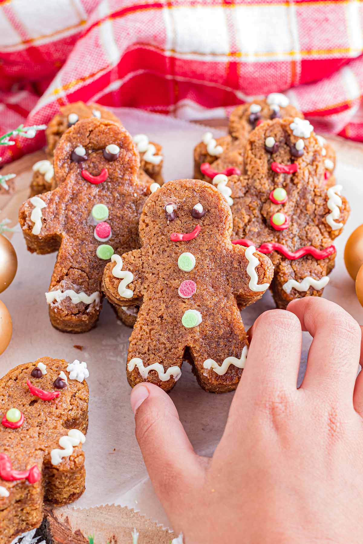 hand holding gingerbread-shaped blondie decorated with icing for eyes, a red smile, and button details.