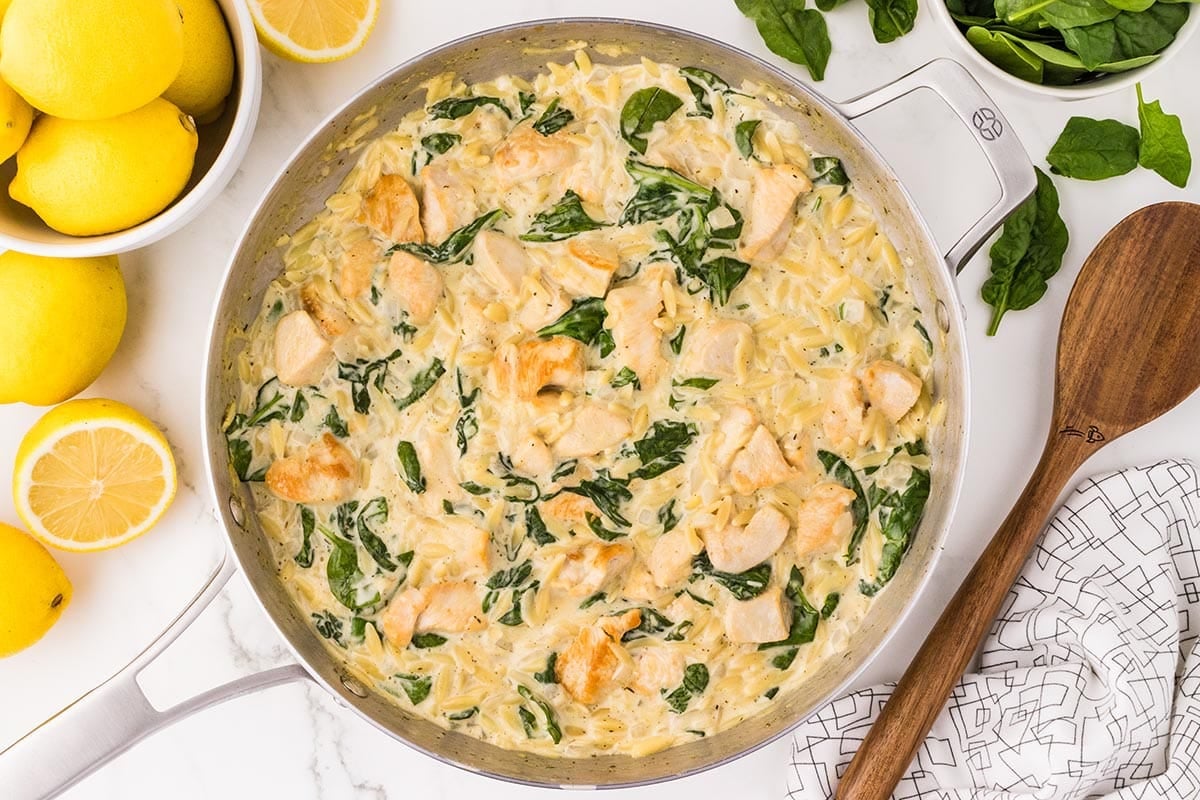 Lemon Chicken Orzo with spinach and creamy sauce in a skillet, garnished with fresh lemons.