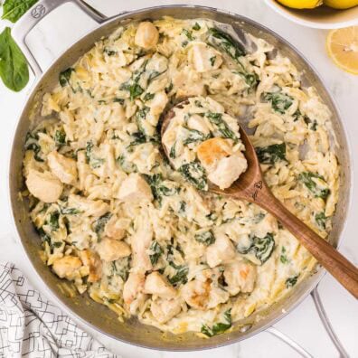 Lemon Chicken Orzo with spinach and creamy sauce in a skillet, served with wooden spoon.