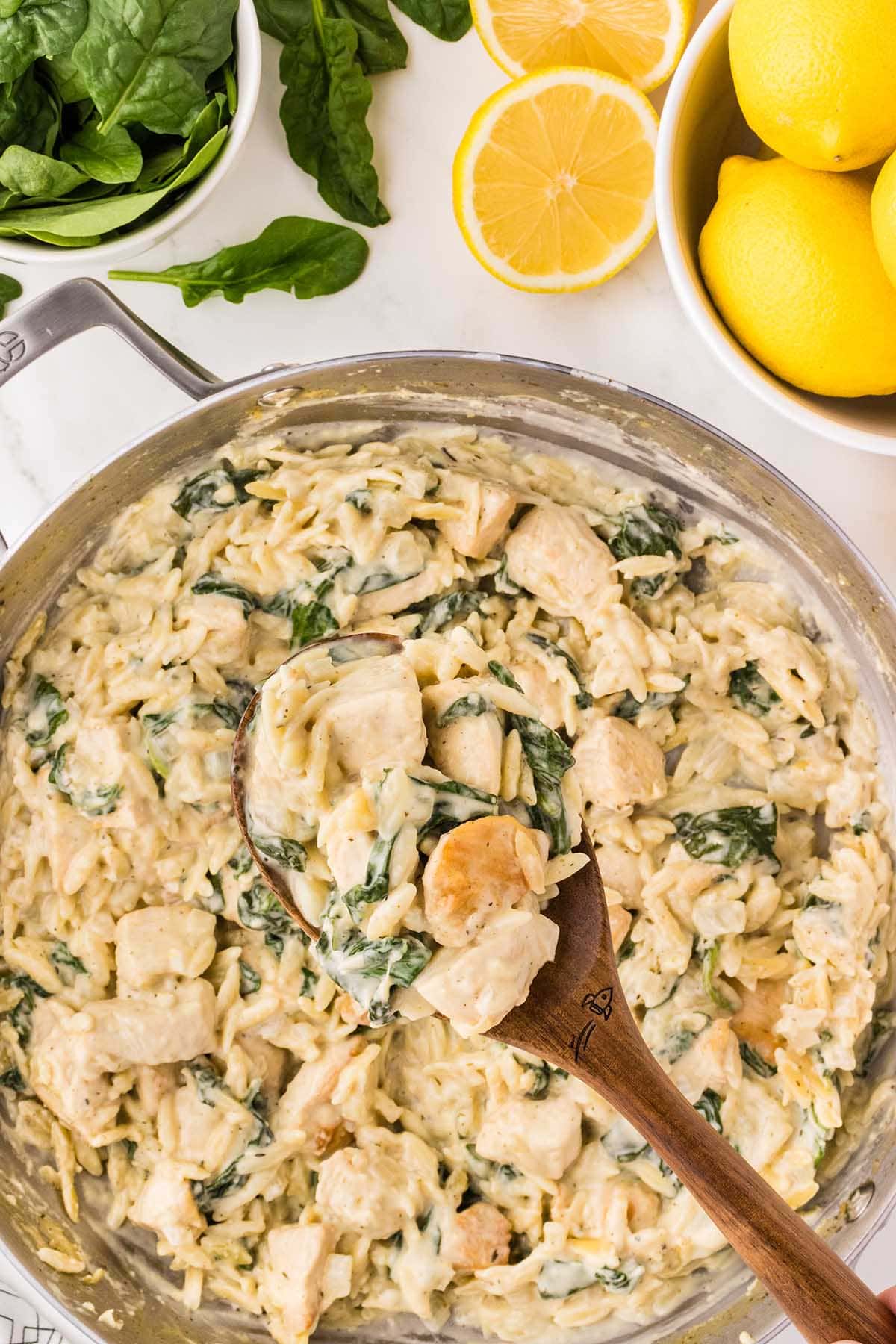 Lemon Chicken Orzo with spinach and creamy sauce in a skillet with a wooden spoon.