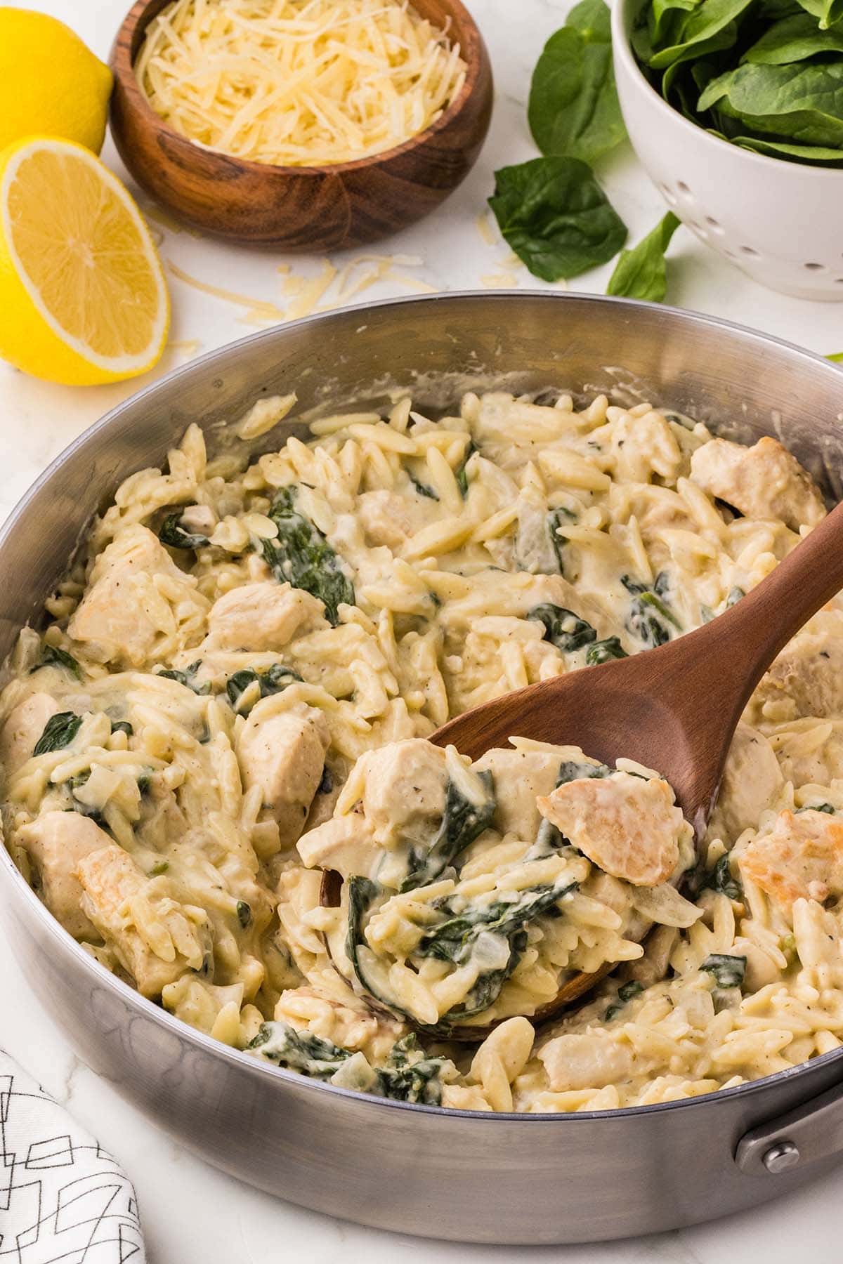 Lemon Chicken Orzo with spinach and creamy sauce in a skillet, topped with Parmesan cheese.