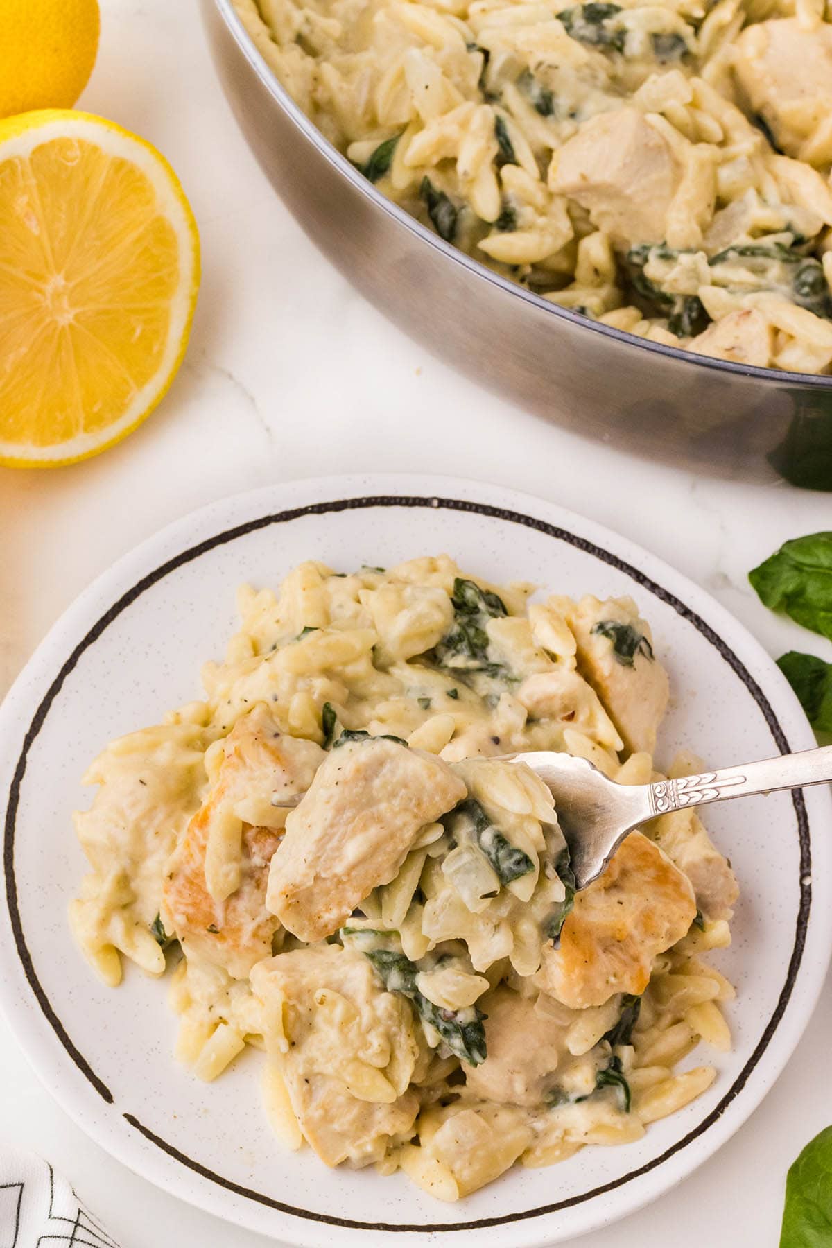 Lemon Chicken Orzo served on a plate with spinach and creamy sauce, garnished with a fork.