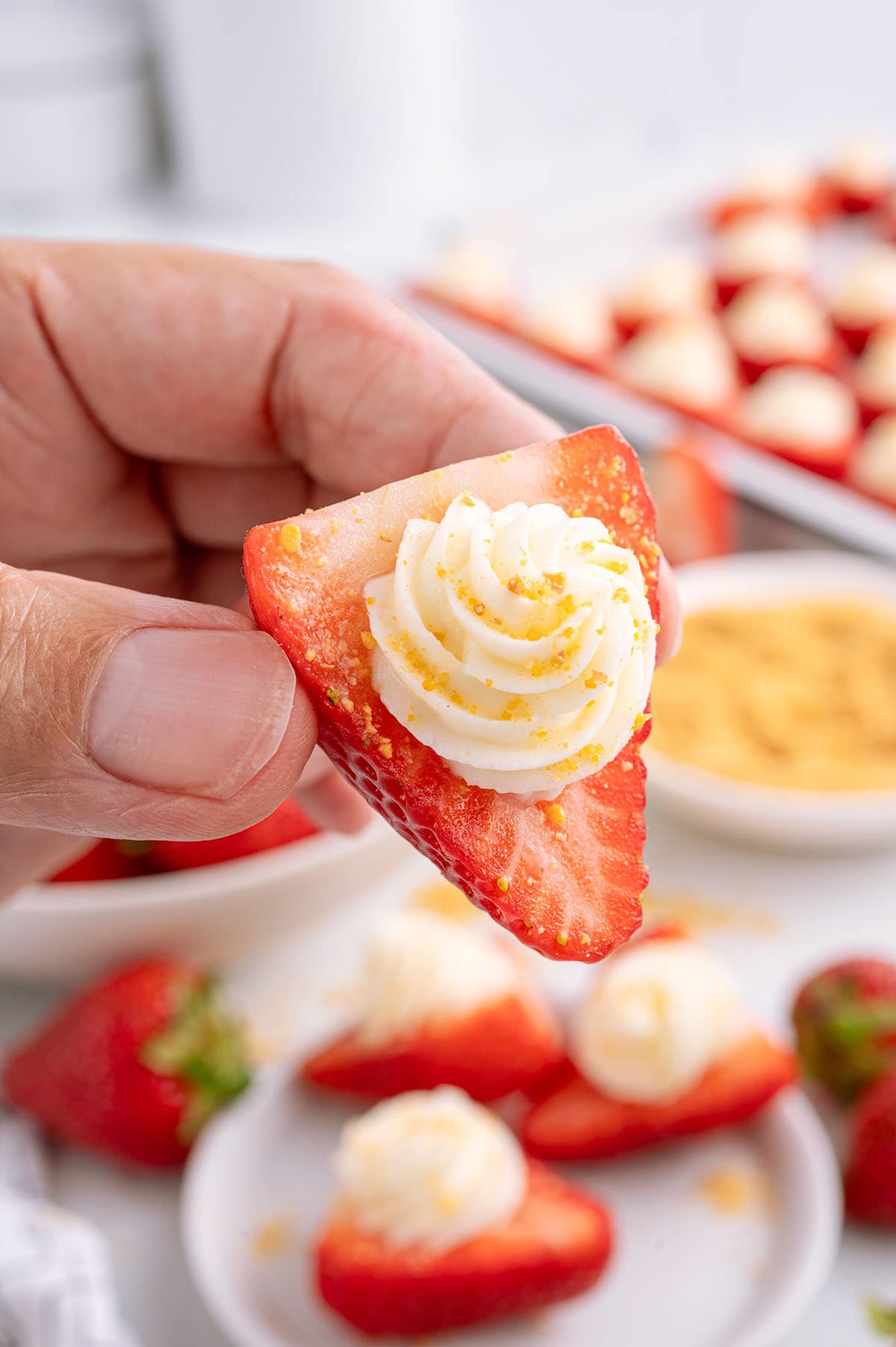 hand holding a deviled strawberries with cream cheese filling and sprinkle of crushed graham cracker crumbs.