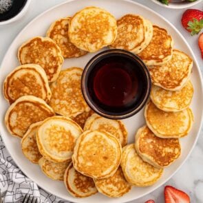 a plate of mini pancakes with a bowl of syrup.