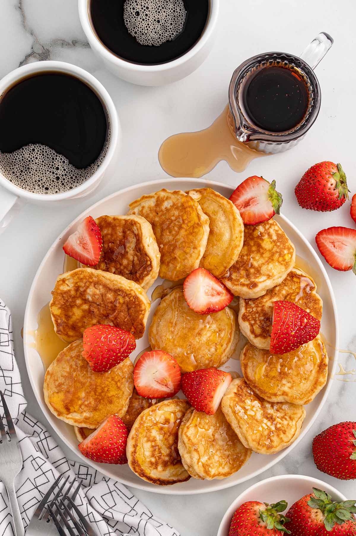 a plate of mini pancakes topped with fresh strawberries.