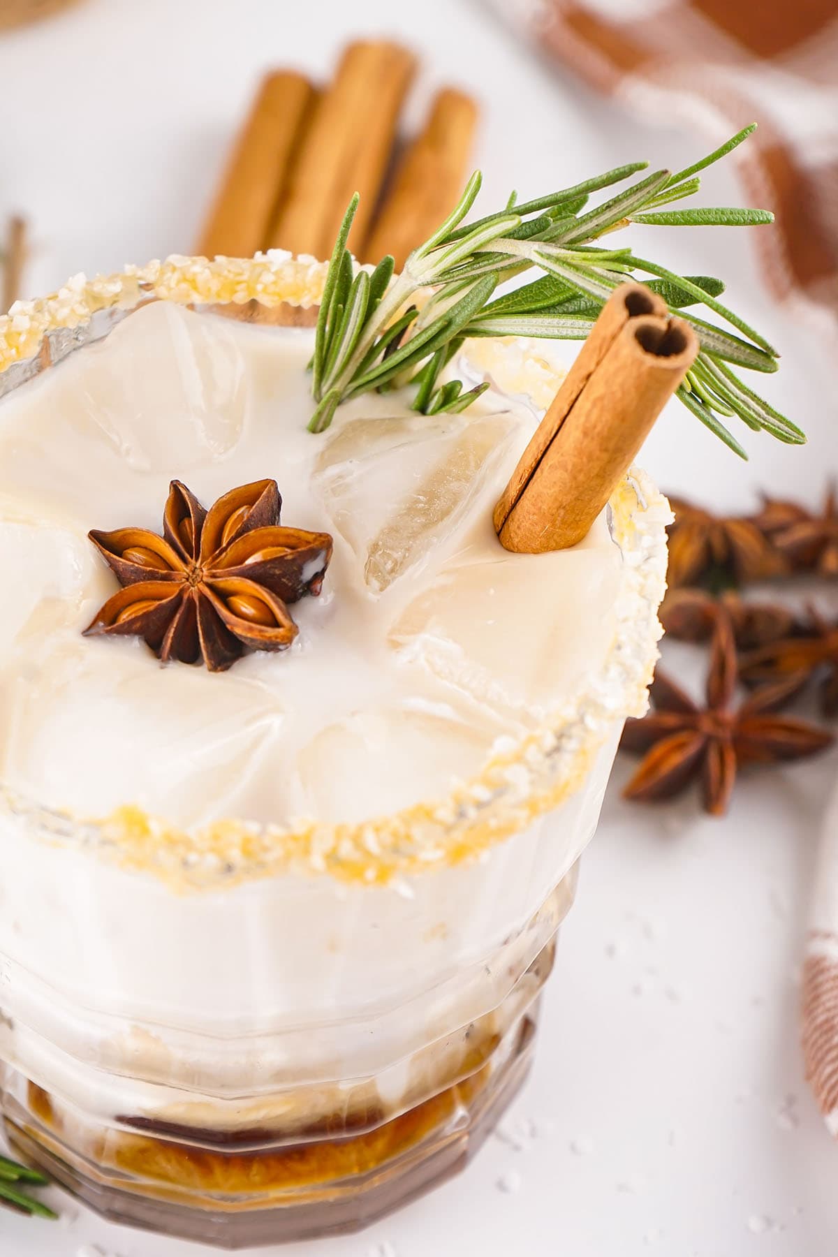 A glass of salted caramel white russian garnished with star anise, cinnamon stick and sprig of rosemary.