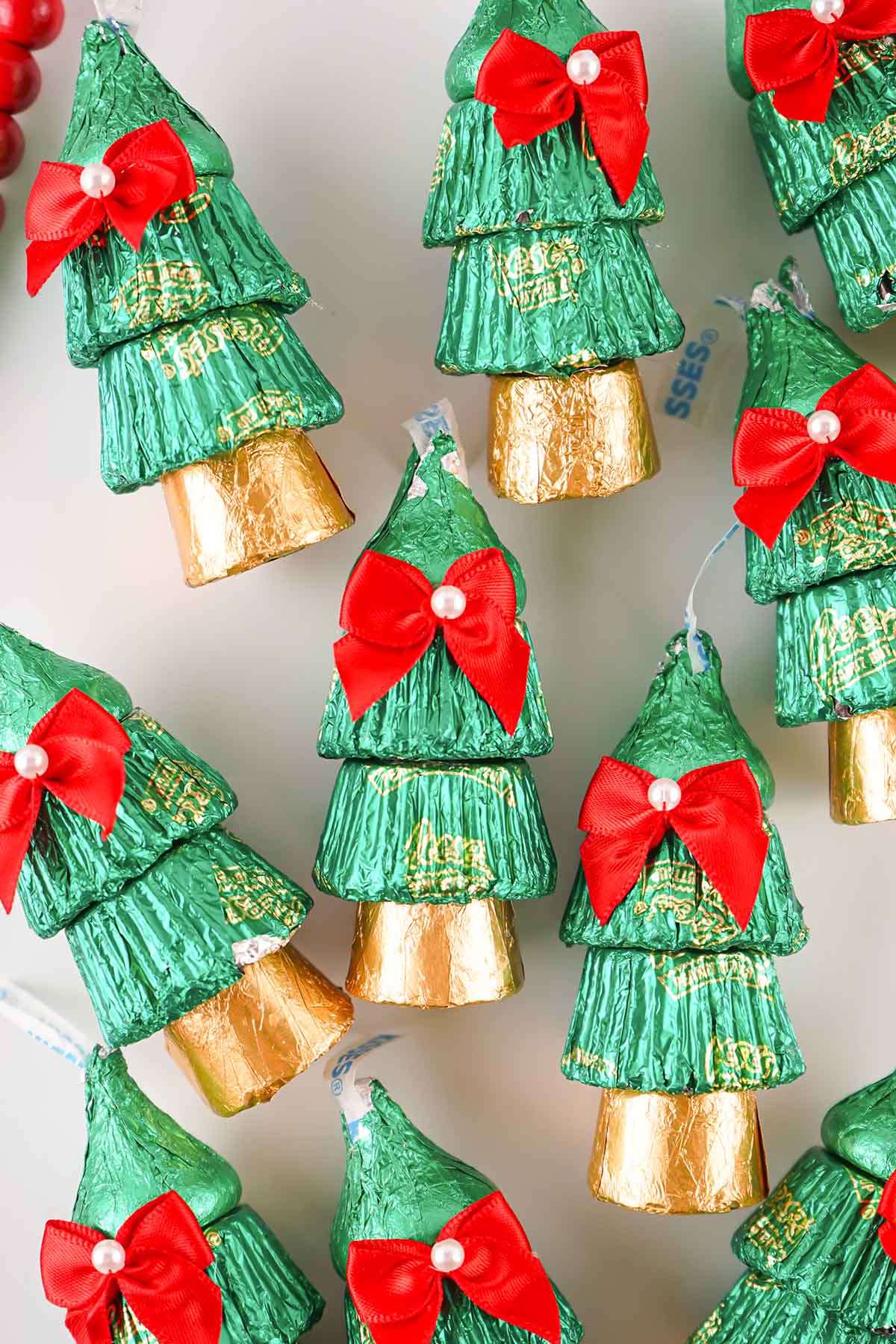 Multiple candy Christmas trees with green and gold foil, red bows, and pearls displayed together.