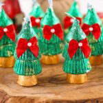 Festive candy Christmas trees wrapped in green and gold foil, decorated with red bows and pearl accents, displayed on a wooden surface.