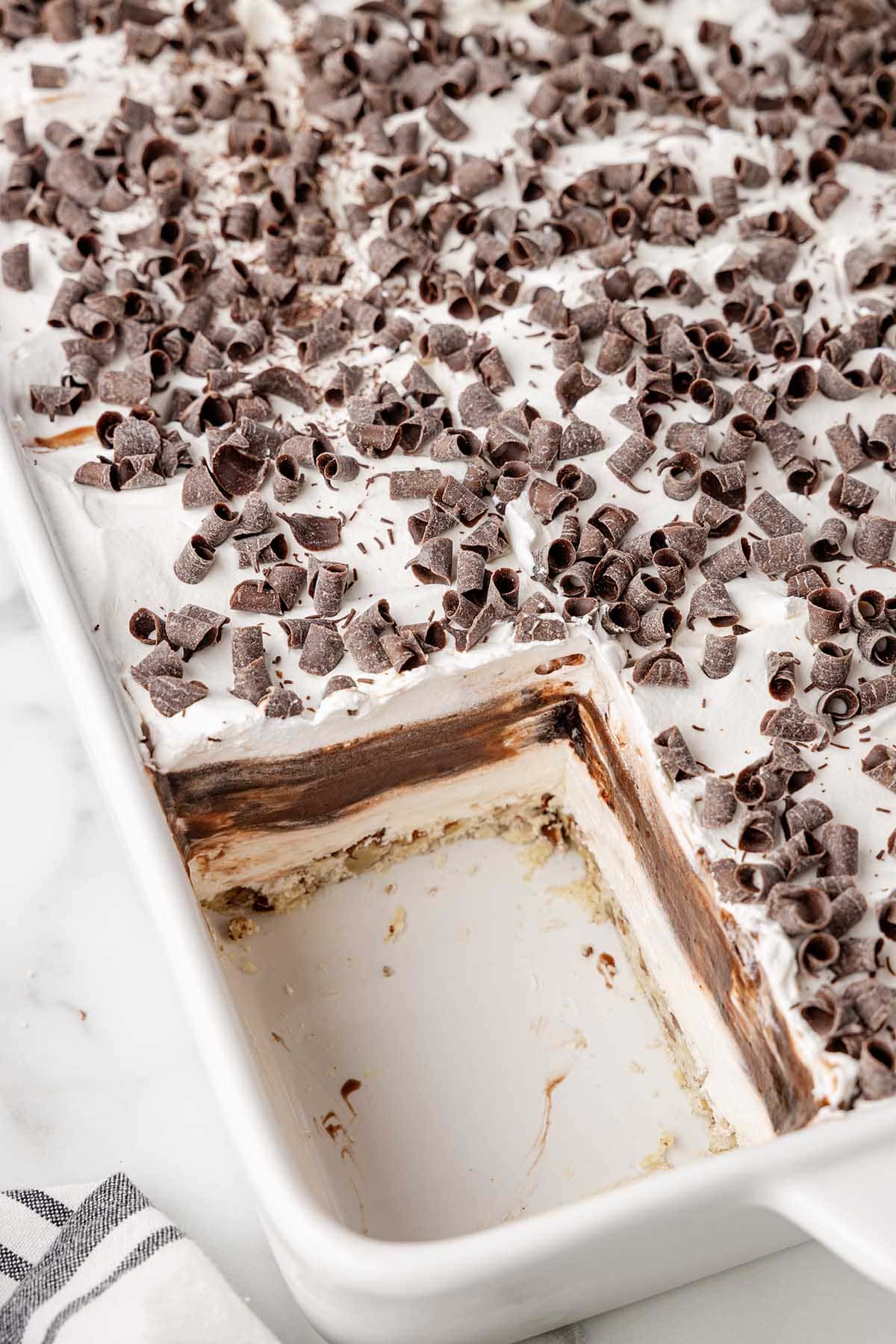 A tray of chocolate delight topped with chocolate curls, with a corner slice removed to reveal the dessert layers.