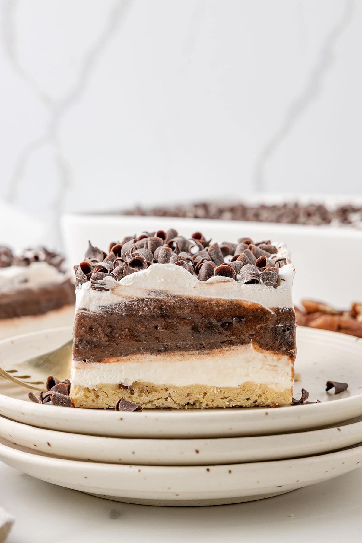 Layered chocolate delight topped with chocolate curls, served on stacked plates.