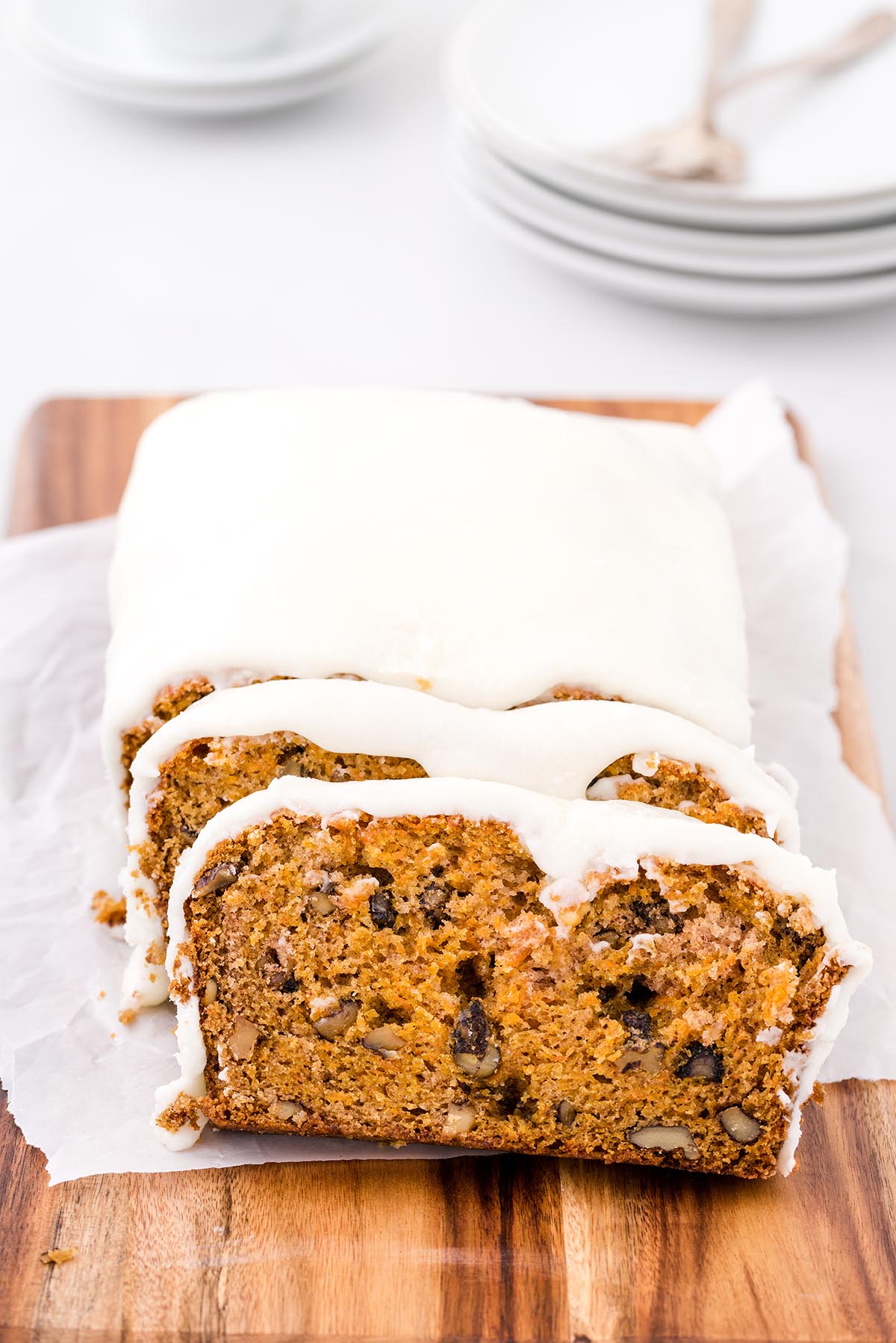 Carrot Bread with a glaze, sliced to reveal a moist interior with walnuts and raisins, on a wooden board lined with parchment.