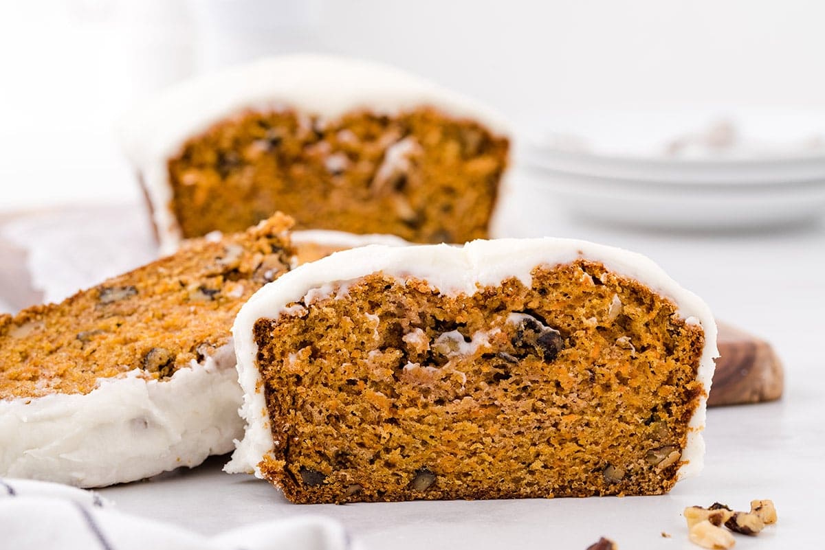 Slices of moist carrot bread topped with a creamy glaze, showing off specks of nuts and carrots.