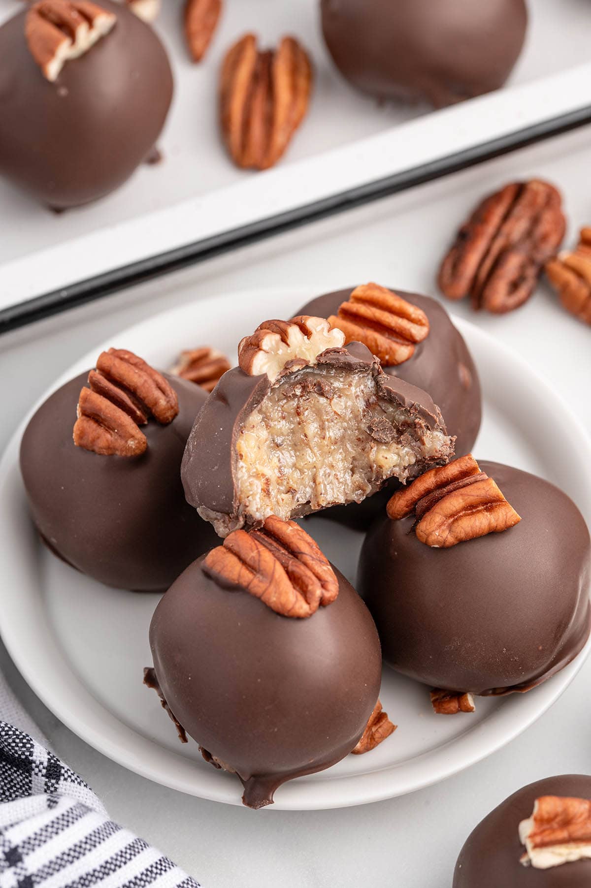 Chocolate-coated condensed milk pecan balls topped with pecans, served on a plate.