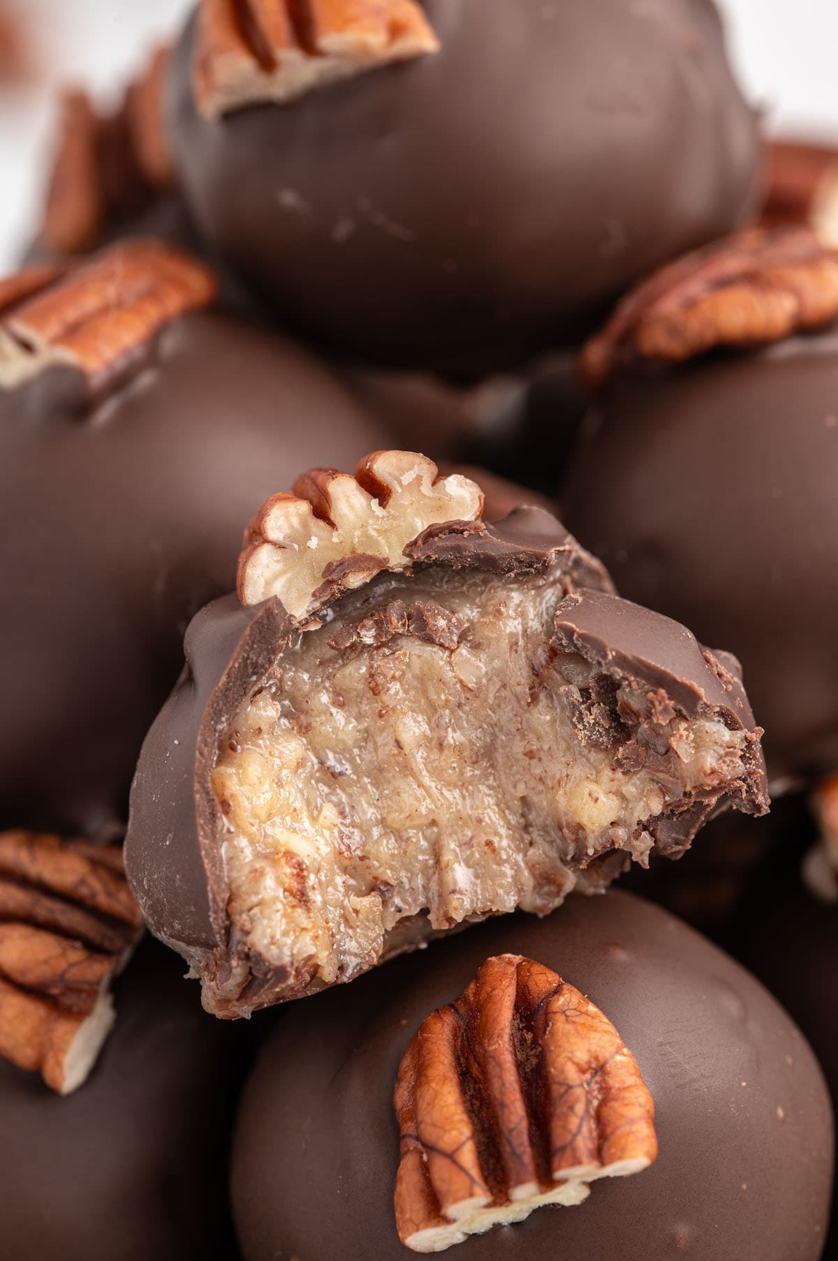 A close-up of a condensed milk pecan ball coated in chocolate, showcasing its creamy pecan-filled center, topped with a pecan piece.