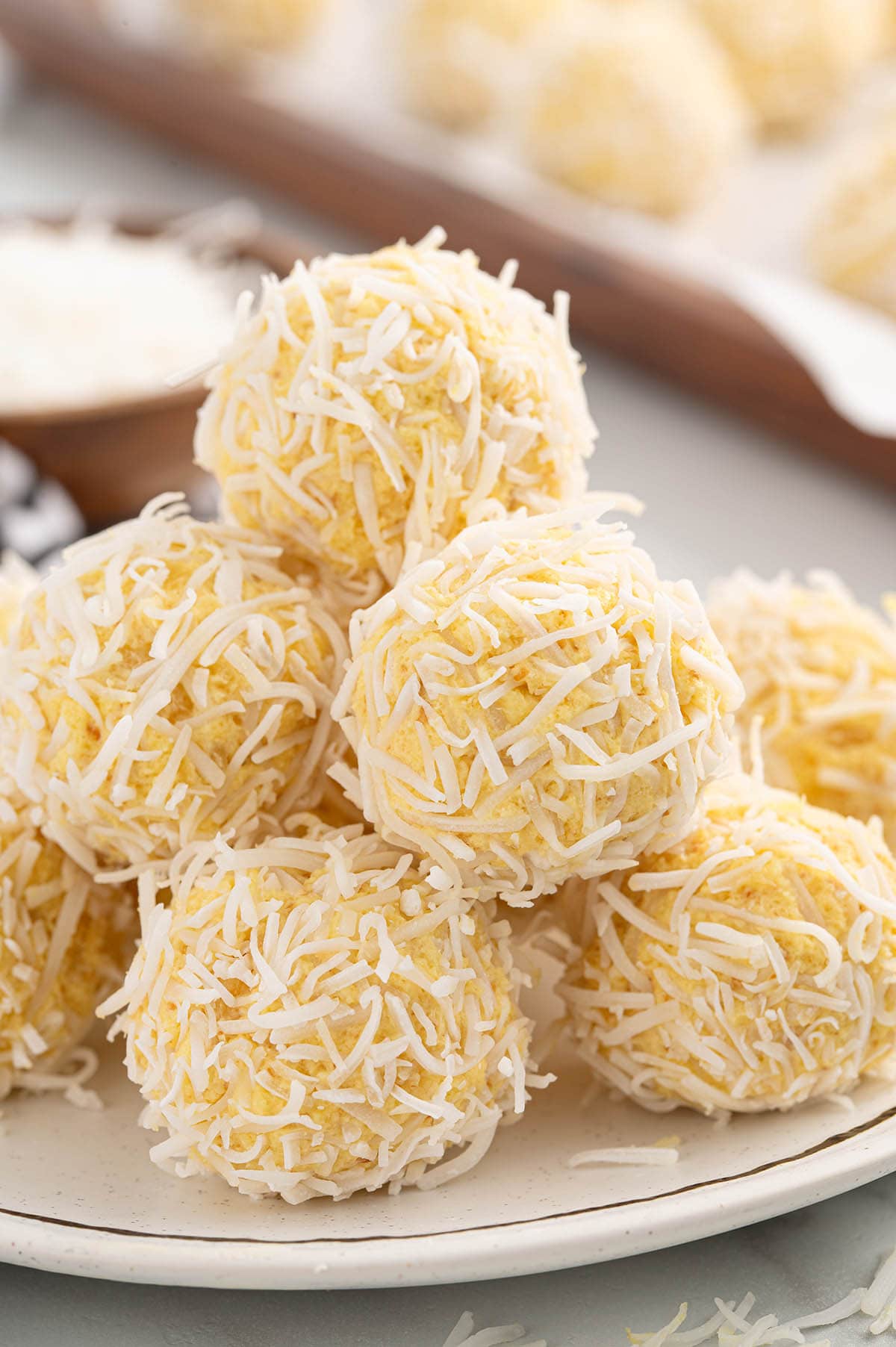 Close-up of pineapple balls coated in shredded coconut, arranged on a plate, with more in the background.