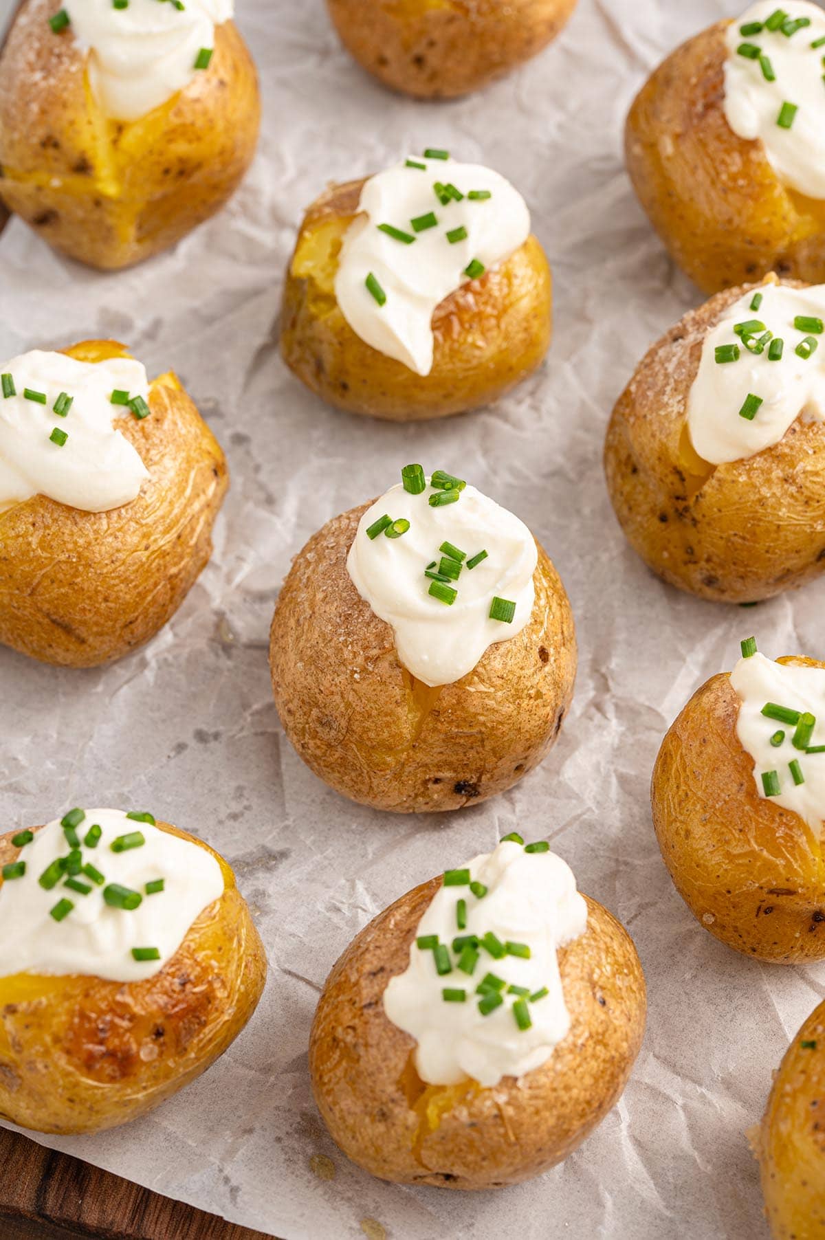 Mini baked potatoes with sour cream on parchment paper.