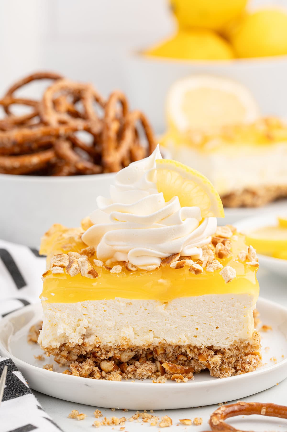 Lemon pretzel dessert slice topped with whipped cream and a lemon wedge.