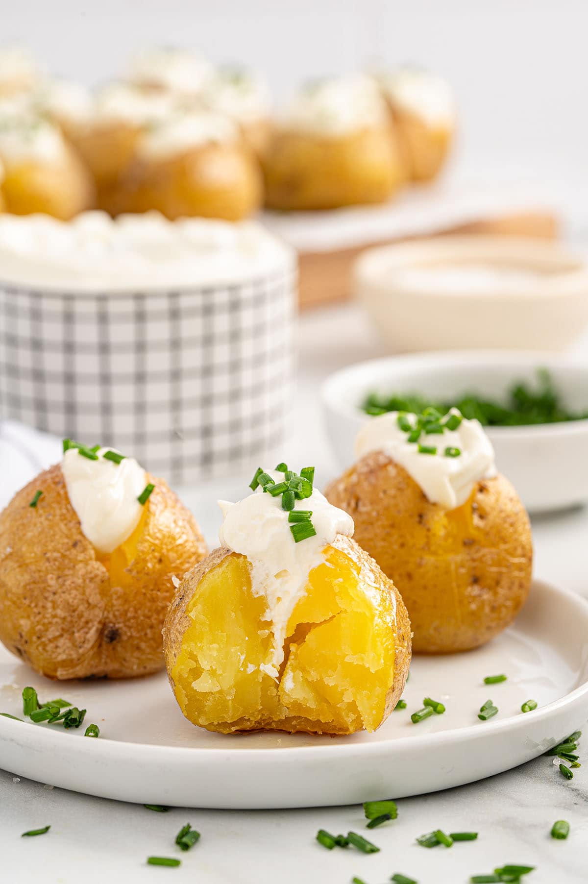 Mini baked potatoes on a plate, topped with sour cream and chopped chives.