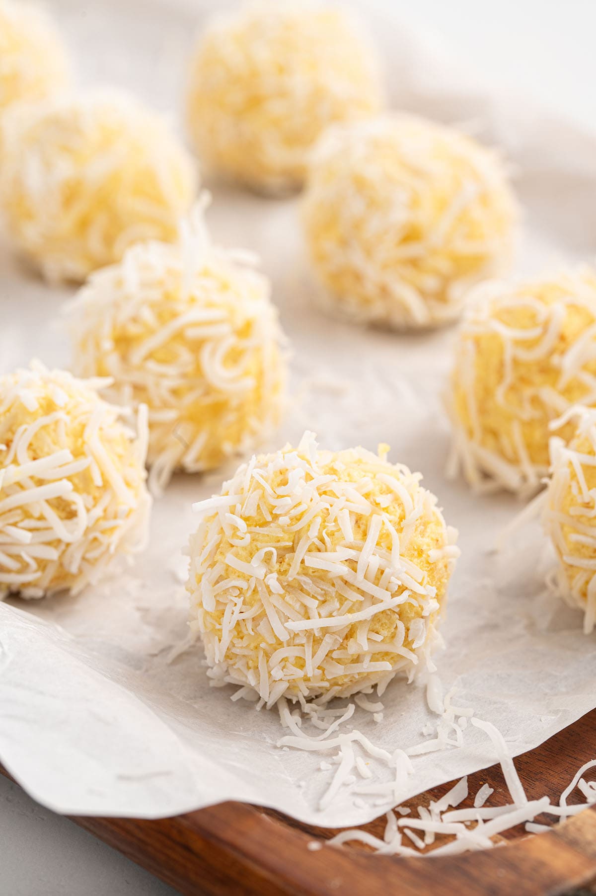 Pineapple balls coated in shredded coconut, arranged on parchment paper on a wooden tray.