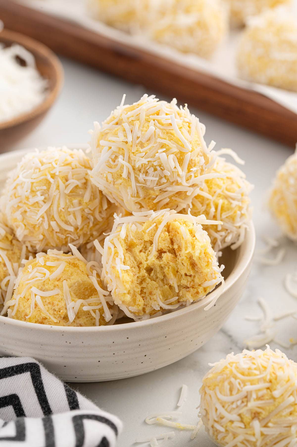 A bowl of pineapple balls rolled in shredded coconut, with one ball bitten. 