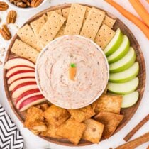 Carrot cake dip surrounded by graham crackers, apple slices, and cinnamon chips.