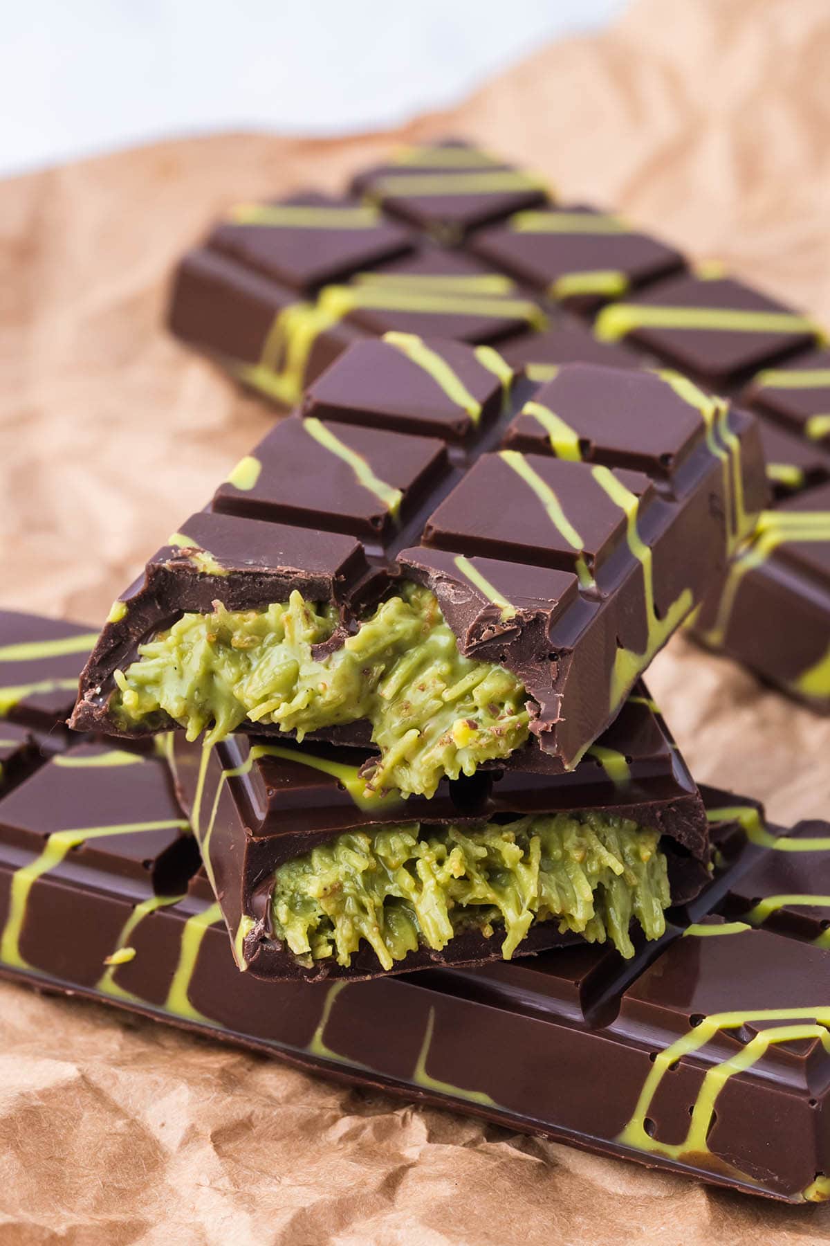 bitten dubai chocolate bars with green kataifi filling and yellow drizzle stacked on parchment paper.